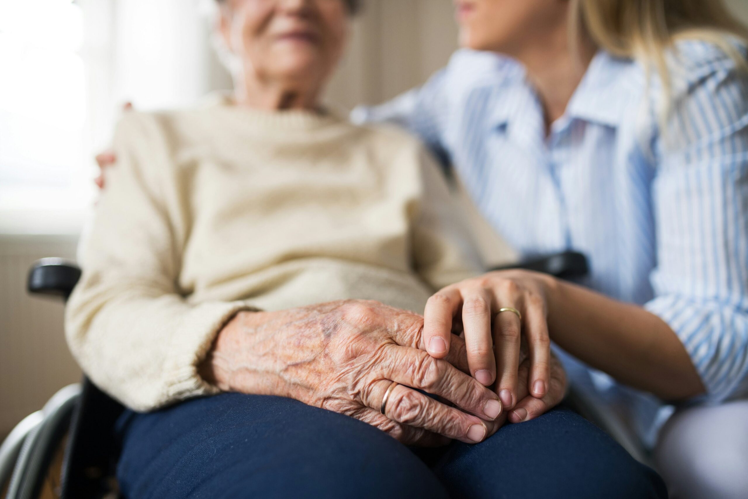Home caregiver gently holding an elderly woman's hands while she sits in a wheelchair