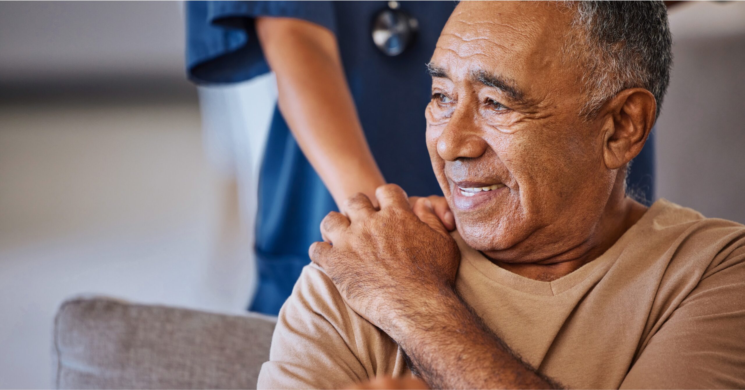 Smiling senior man holding a private duty nurse's hand on his shoulder during in-home nursing care