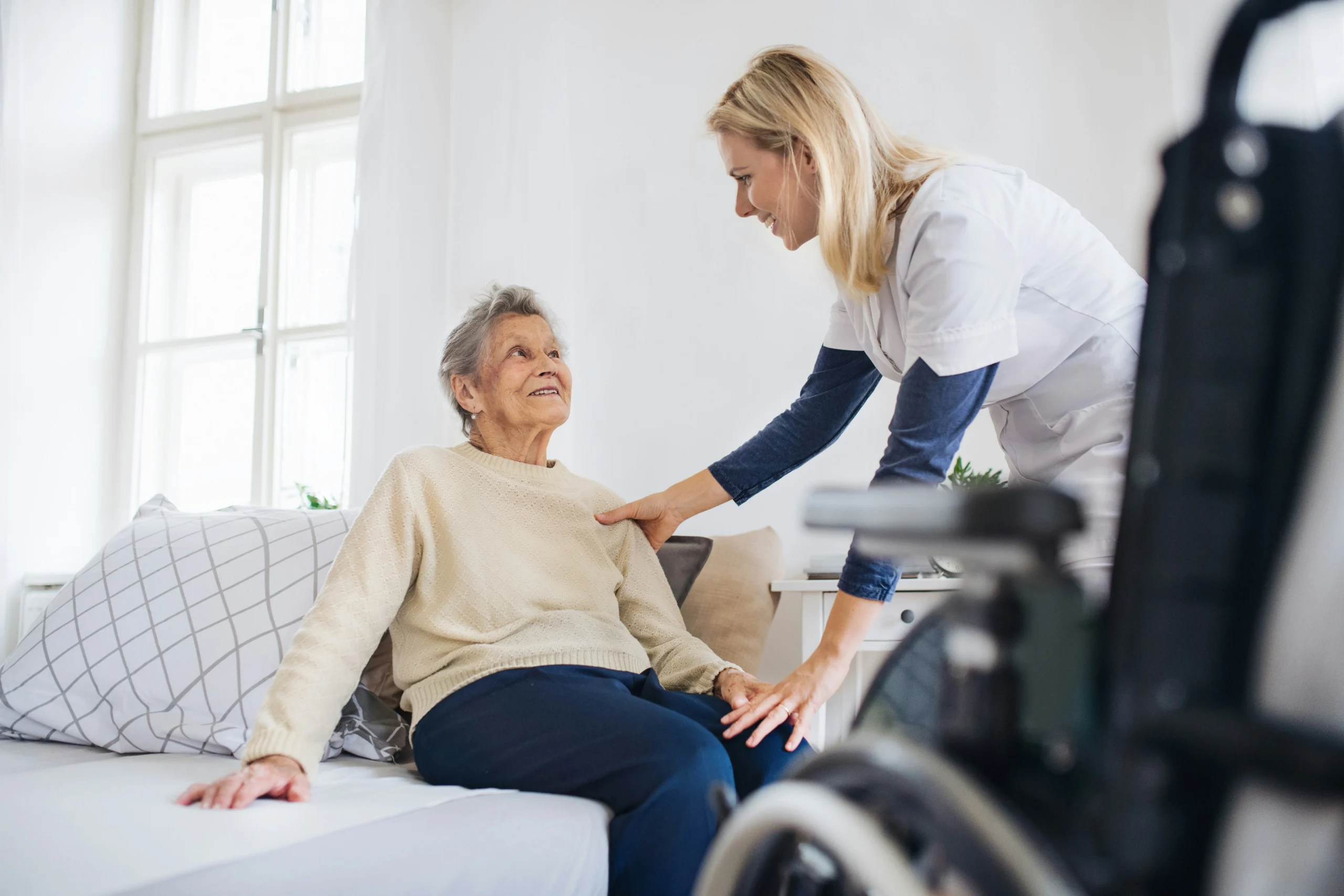 Home care aide helping a senior woman stand from her bed at home during hip replacement recovery